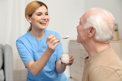 nurse feeding elderly man with yogurt